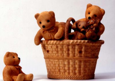 Soft, fuzzy looking teddy bears in a wicker basket, all carved from wood by De Marchi.