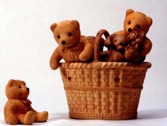 Soft, fuzzy looking teddy bears in a wicker basket, all carved from wood by De Marchi. 