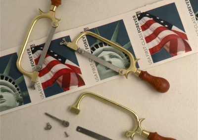 Miniature hand saws on top of a roll of stamps.