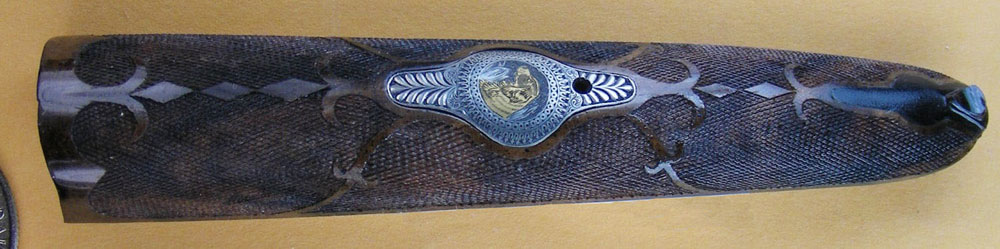 An engraved and inlaid metal plate is inset on the forearm plate.