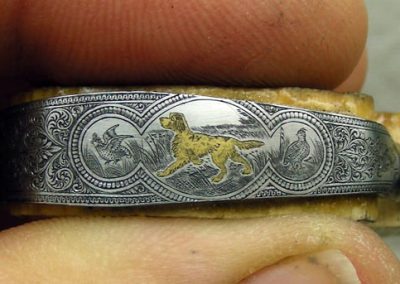 The unfinished trigger guard, with birds and an inlaid gold hunting dog.