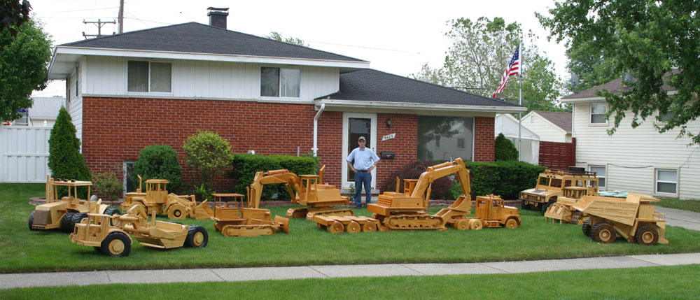 Chuck Hoggarth standing in front of his home with his collection of large scale construction equipment models. 