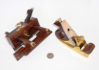 A miniature brass plow plane modeled in wood and brass, and a brass Norris style smoother.