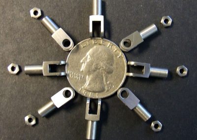 Eight stainless steel clevises and nuts for the pushrod ends surround a quarter for scale.