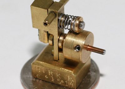 Birk’s mini steam engine is photographed sitting atop a US quarter to show its extremely small size.