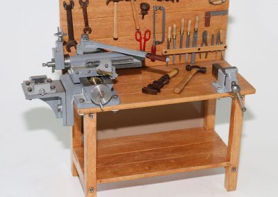 This tiny wooden workbench features a hand operated metal shaper attached to the bench top.