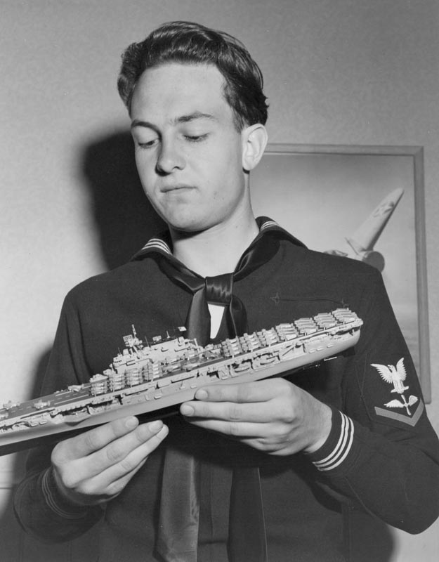 Bill in his Navy uniform with a scale model aircraft carrier. 