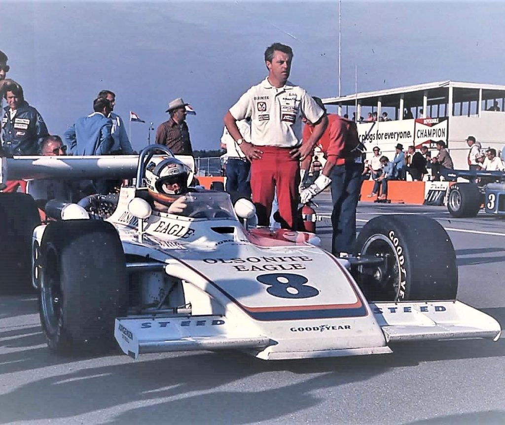 Butch Wilson stands beside Bobby Unser, who is at the wheel of the IndyCar.